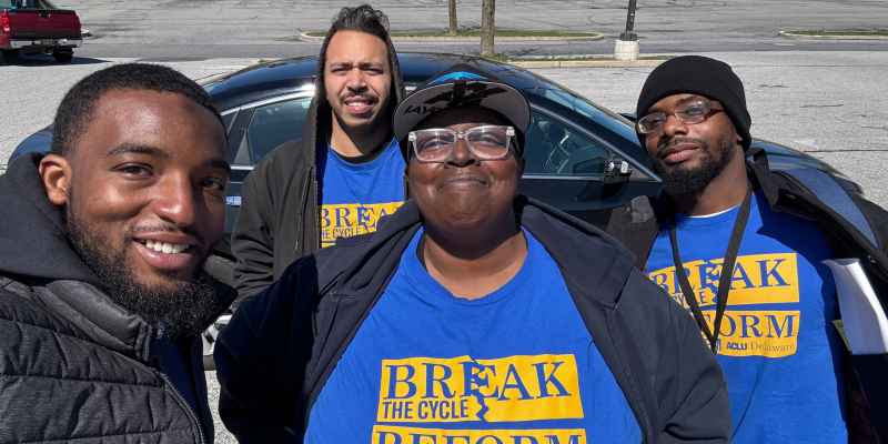 Four people standing in a parking lot with matching blue shirts