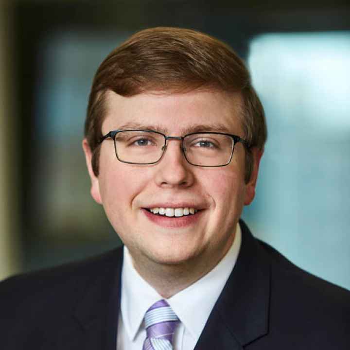 A portrait headshot of David Fry, wearing a suit and a purple and blue striped tie.